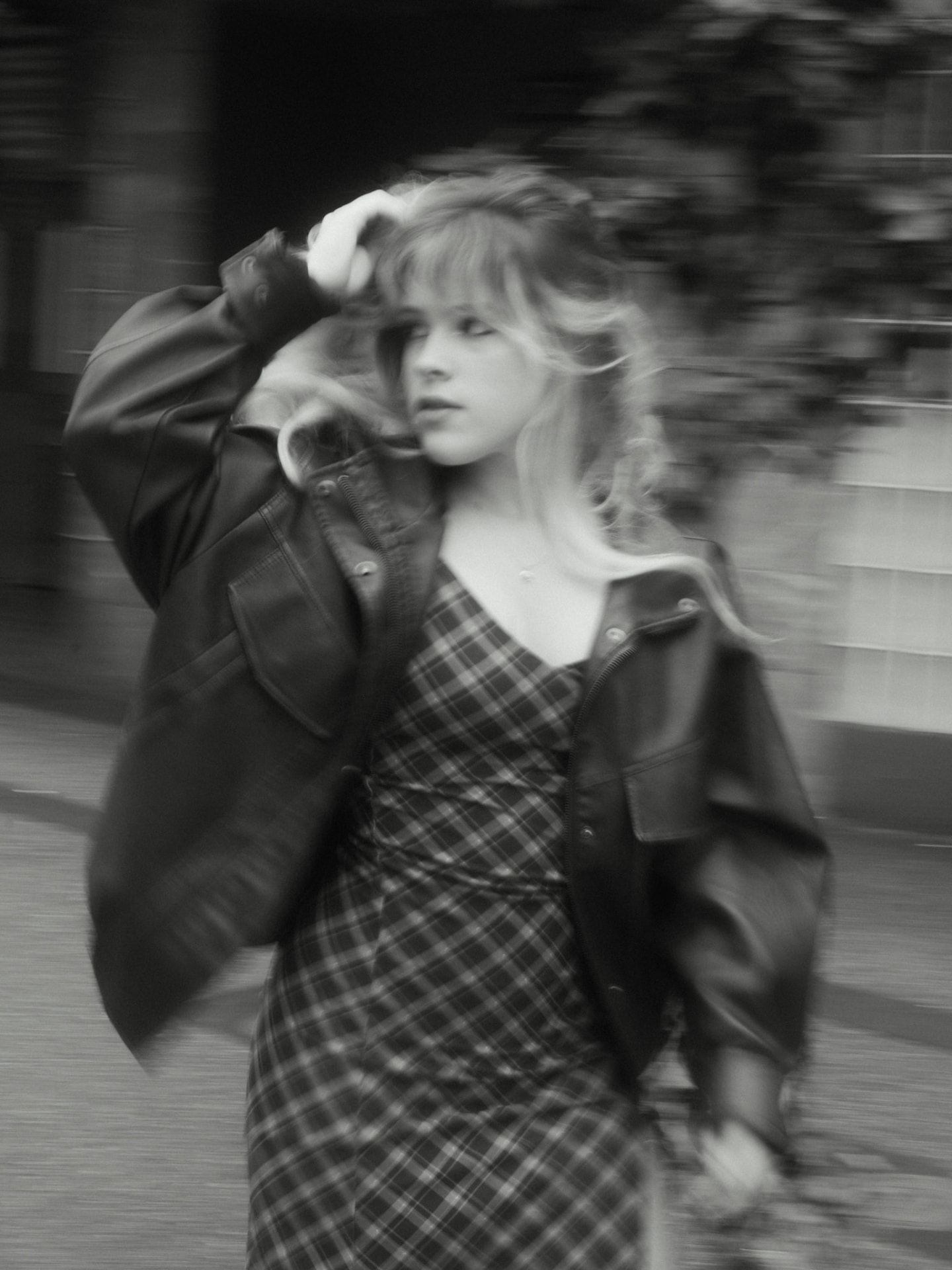 Black and white motion portrait of a woman walking and turning in a plaid dress and leather jacket in Metro Vancouver