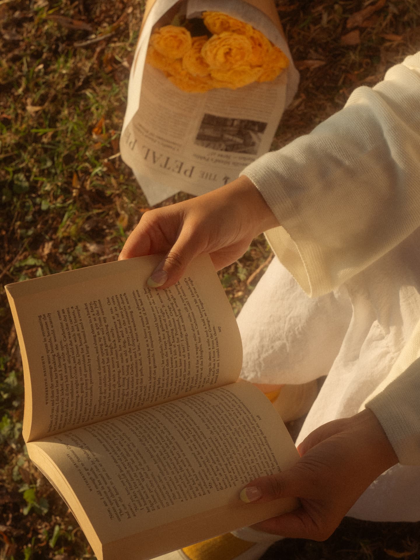 Close-up of hands holding an open book on the grass beside a bouquet of yellow roses in Metro Vancouver