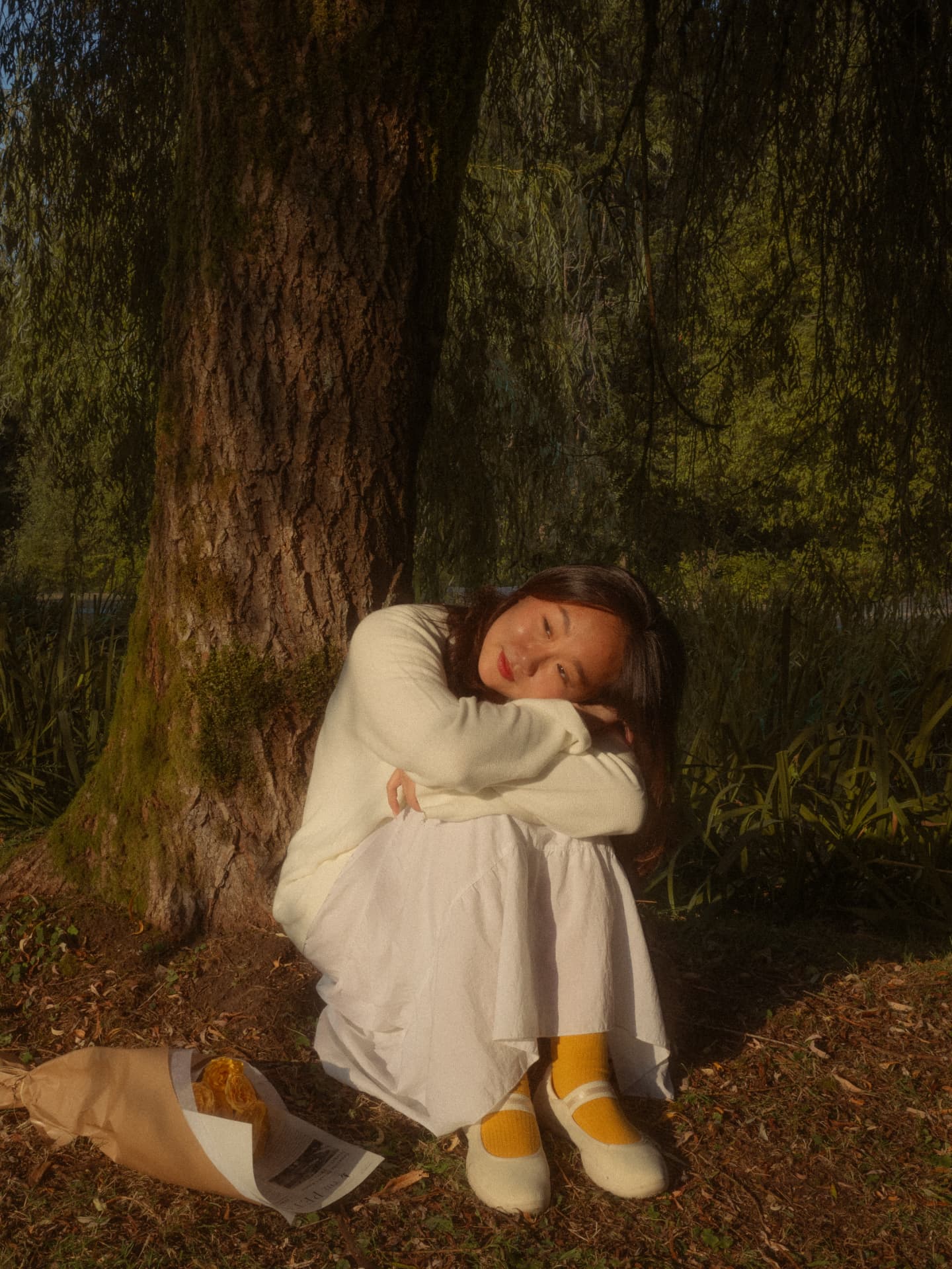 Woman seated at the base of a tree resting her head on her knees in a contemplative Metro Vancouver scene