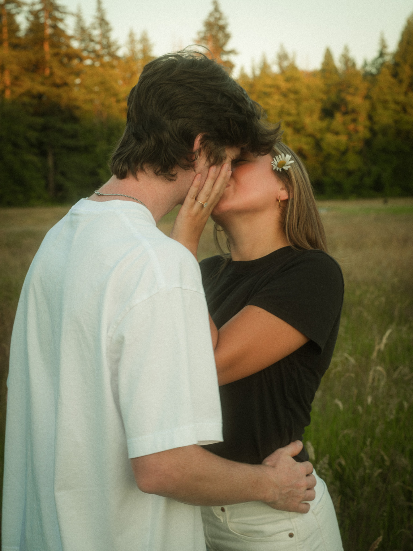 Couple kissing at sunset in a Metro Vancouver field with a daisy in her hair