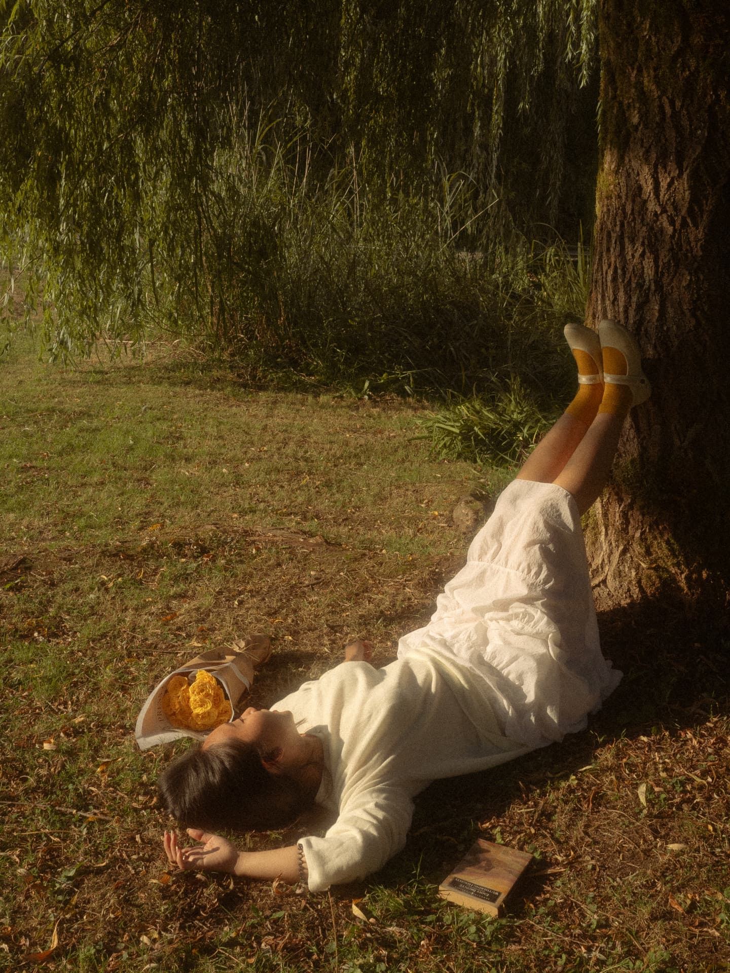 Woman lying on the grass with her legs propped against a tree trunk in a relaxed, dreamy Metro Vancouver scene