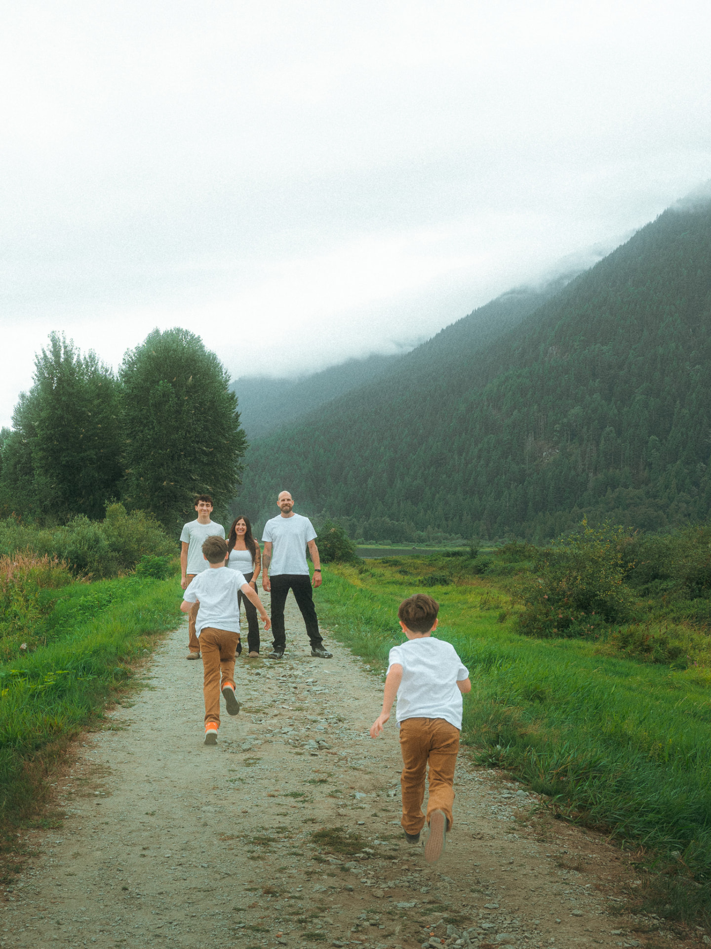 Two young boys running toward their waiting family on a dirt path in a lush, foggy mountain landscape near Metro Vancouver