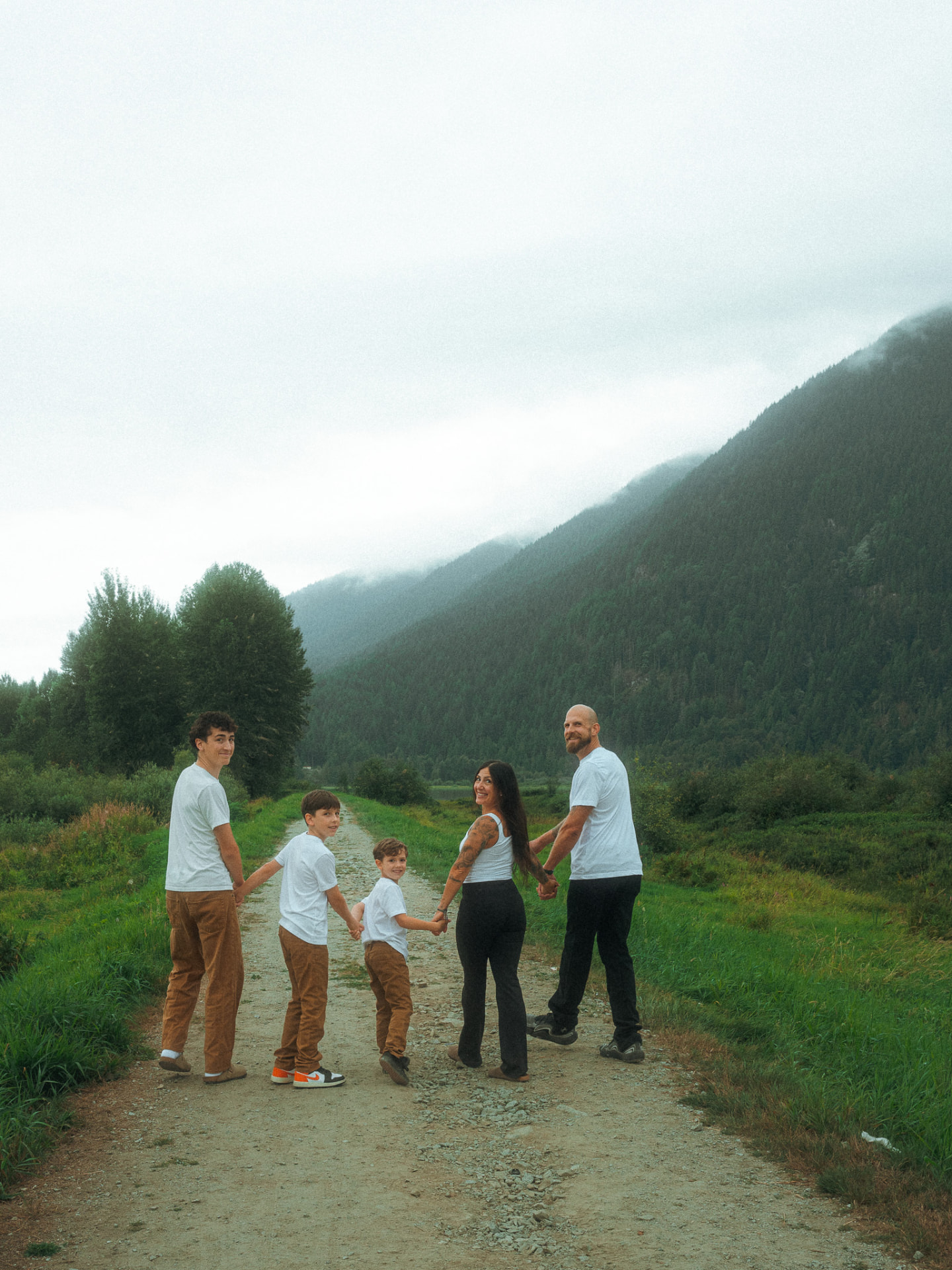 Family of five holding hands on a mountain trail near Metro Vancouver, turning back with happy smiles