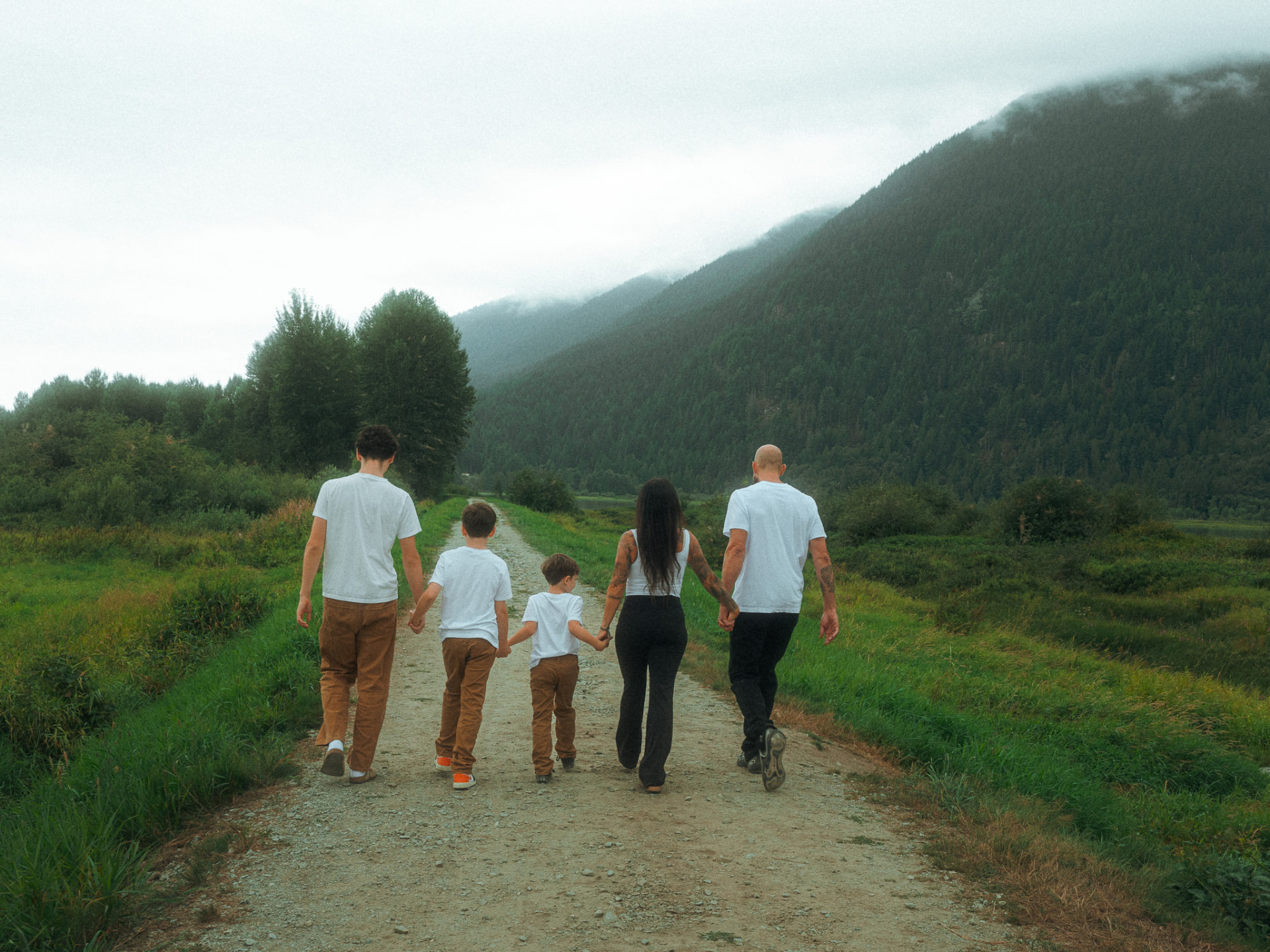 Family of five walking hand-in-hand down a dirt trail toward misty peaks near Metro Vancouver