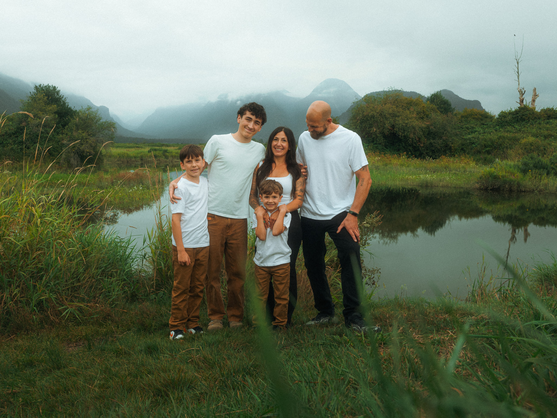 Family of five standing together beside a pond with misty mountains in the background near Metro Vancouver