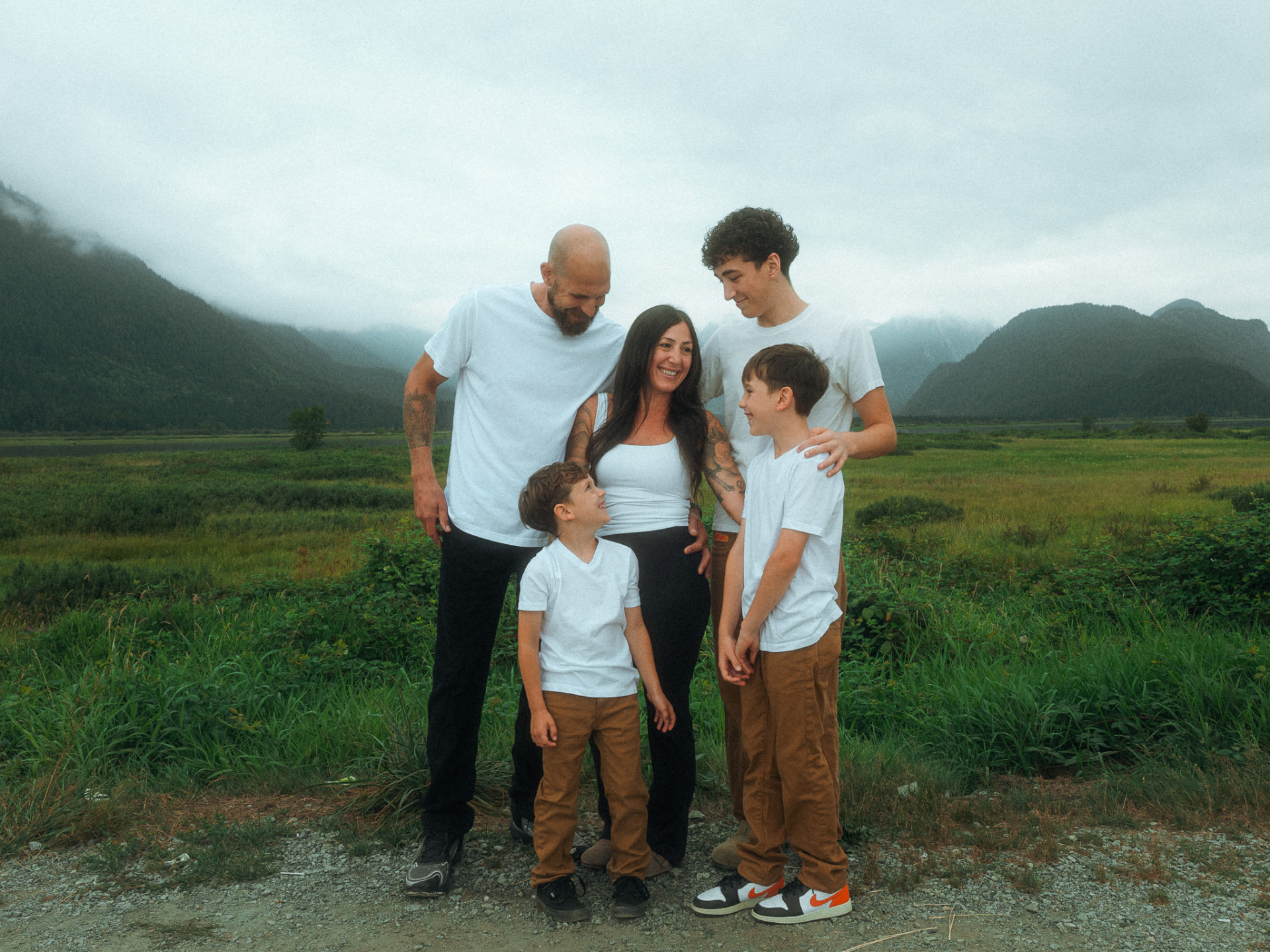 Family of five laughing together in a green mountain valley near Metro Vancouver under a soft overcast sky