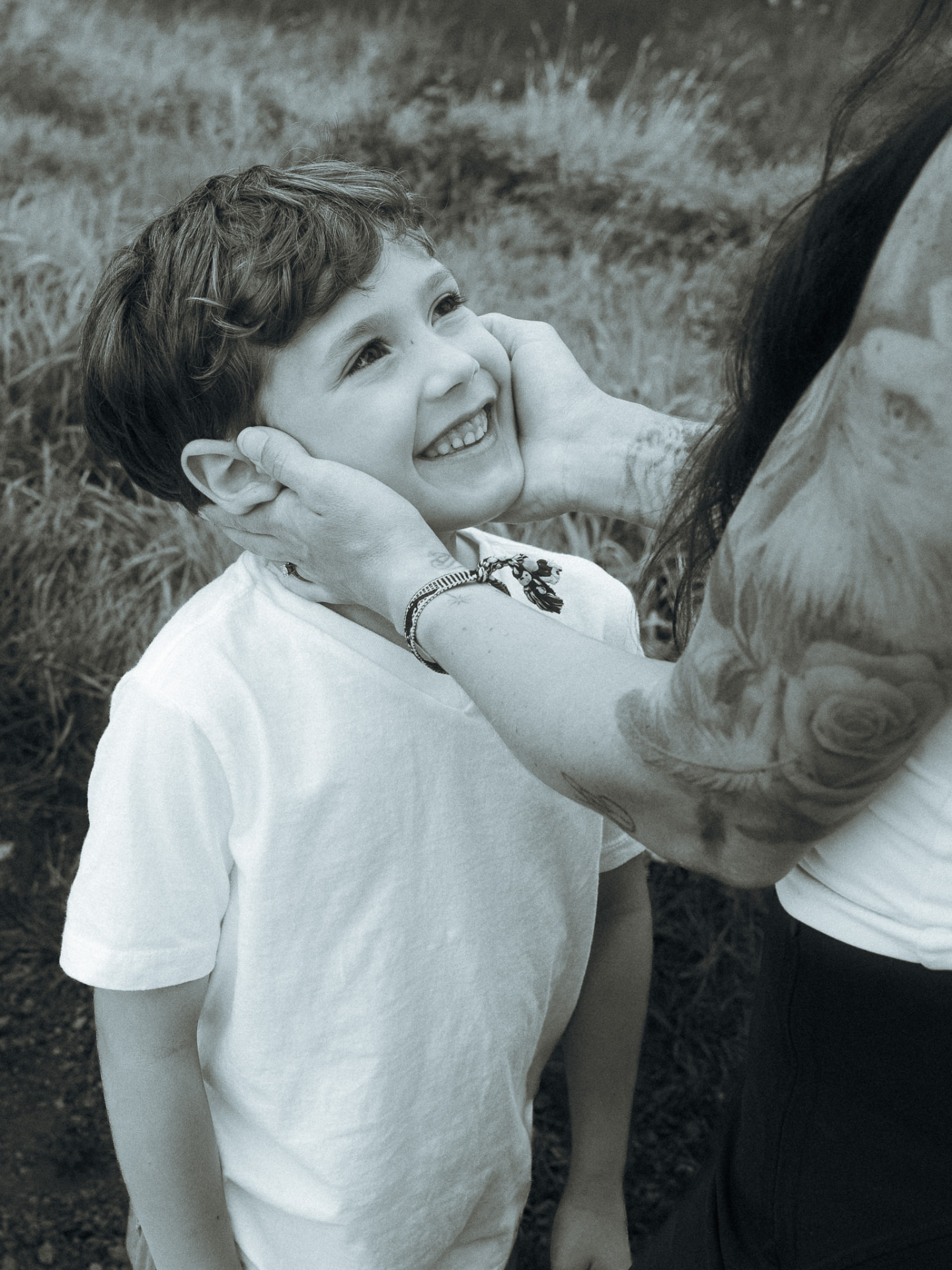 Black and white close-up of a mother cupping her young son's face in a grassy field near Metro Vancouver