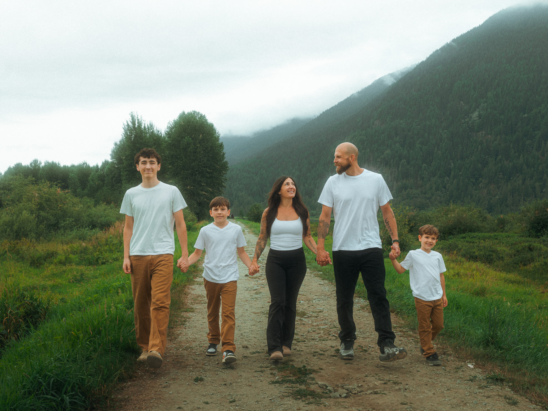Family of five walking hand-in-hand down a dirt path in a misty mountain valley near Metro Vancouver