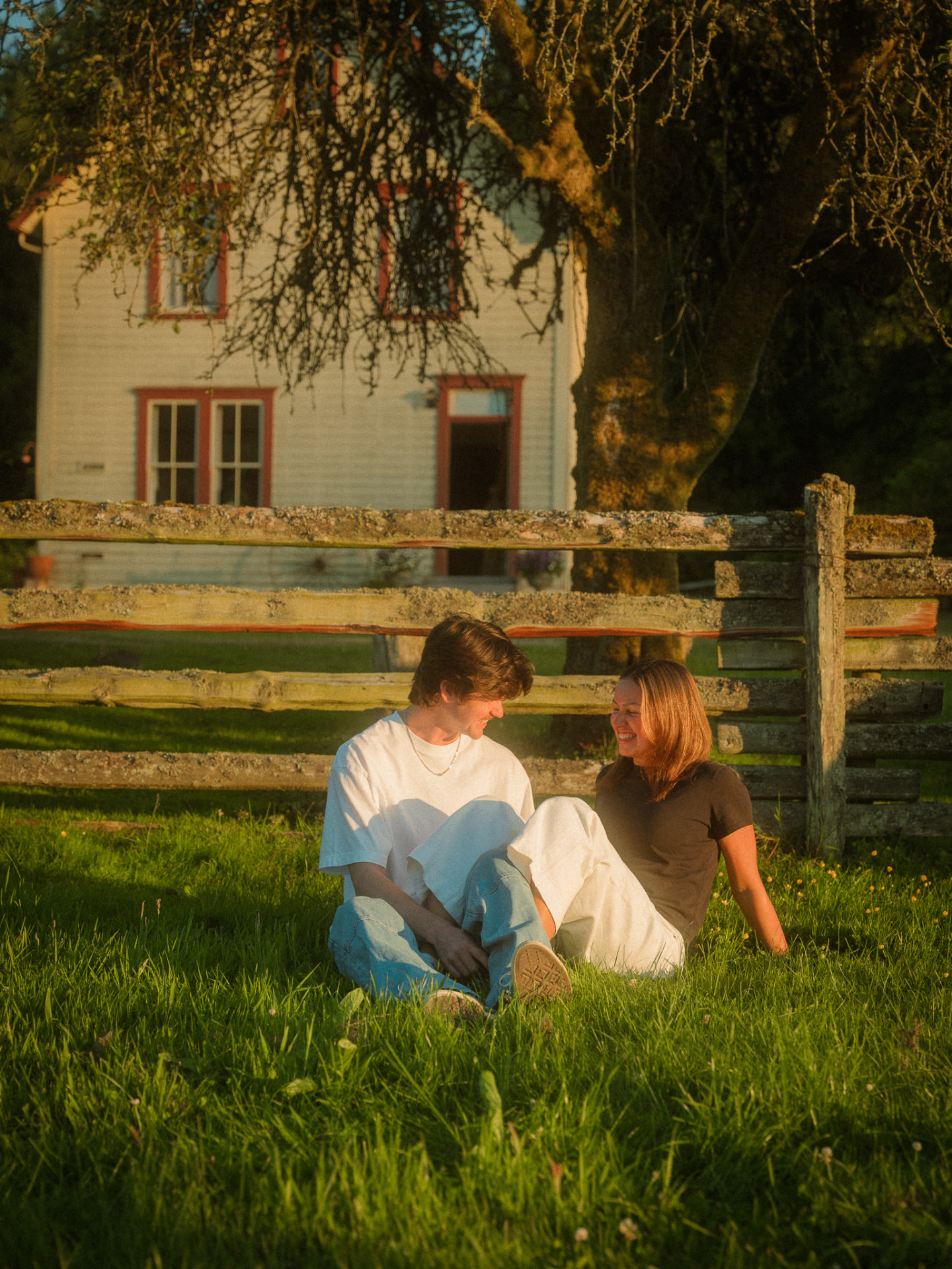 Couple sitting on the grass in front of a heritage farmhouse at golden hour, Metro Vancouver