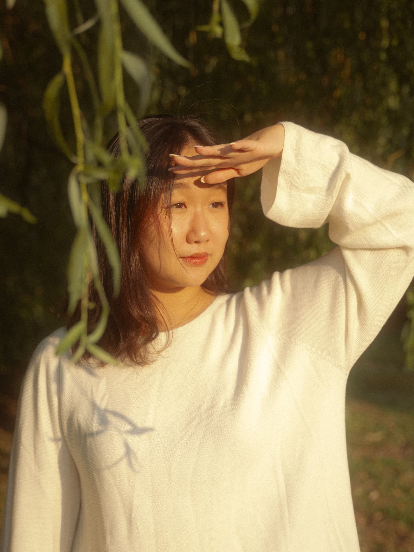 Young woman in a white sweater shielding her eyes from the sun in a bright, leafy Metro Vancouver setting