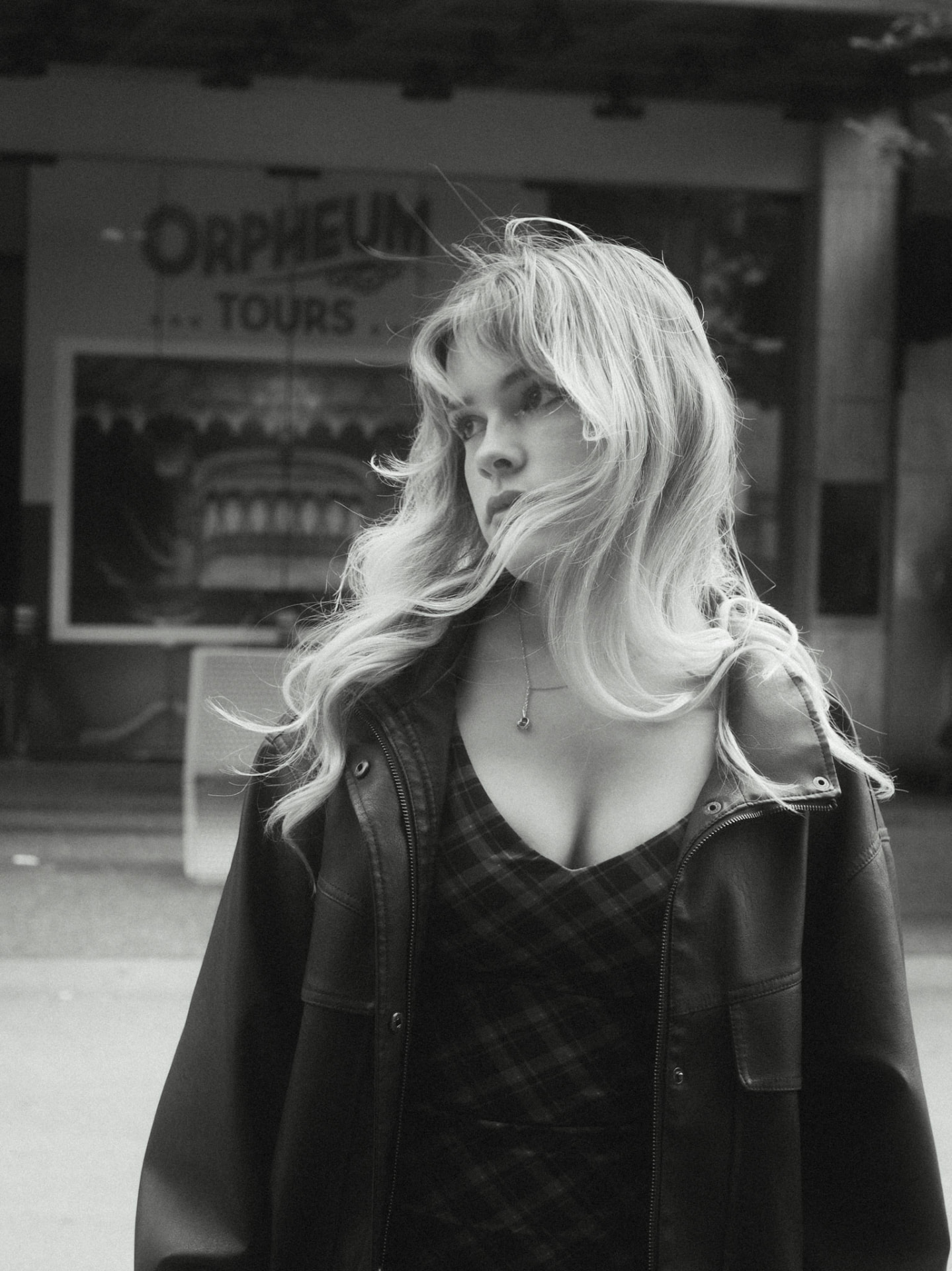 Black and white candid of a woman in a plaid dress and leather jacket with wind-blown hair on a Metro Vancouver street