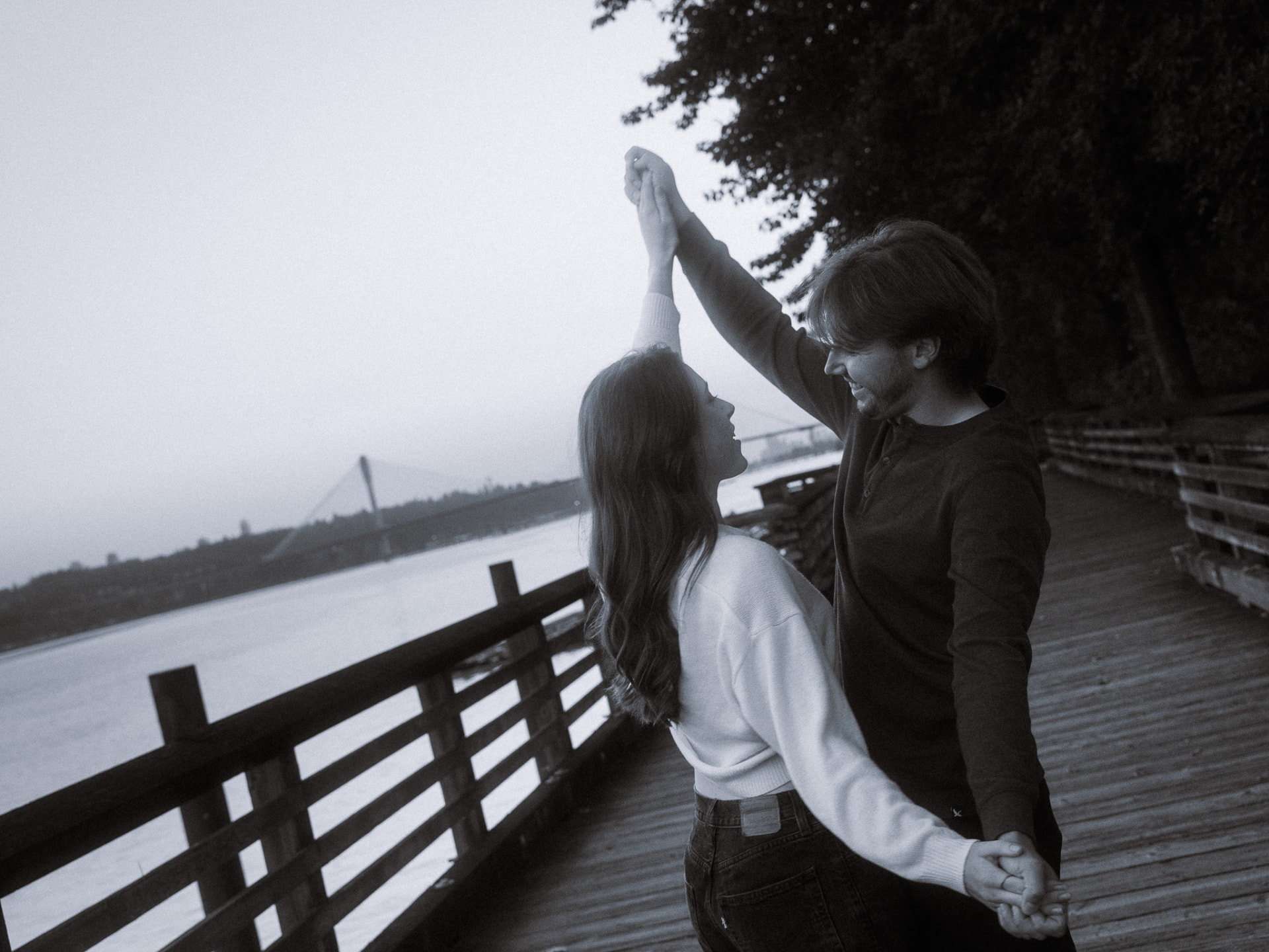 Black and white photo of a couple dancing on a wooden boardwalk by the water at twilight in Metro Vancouver