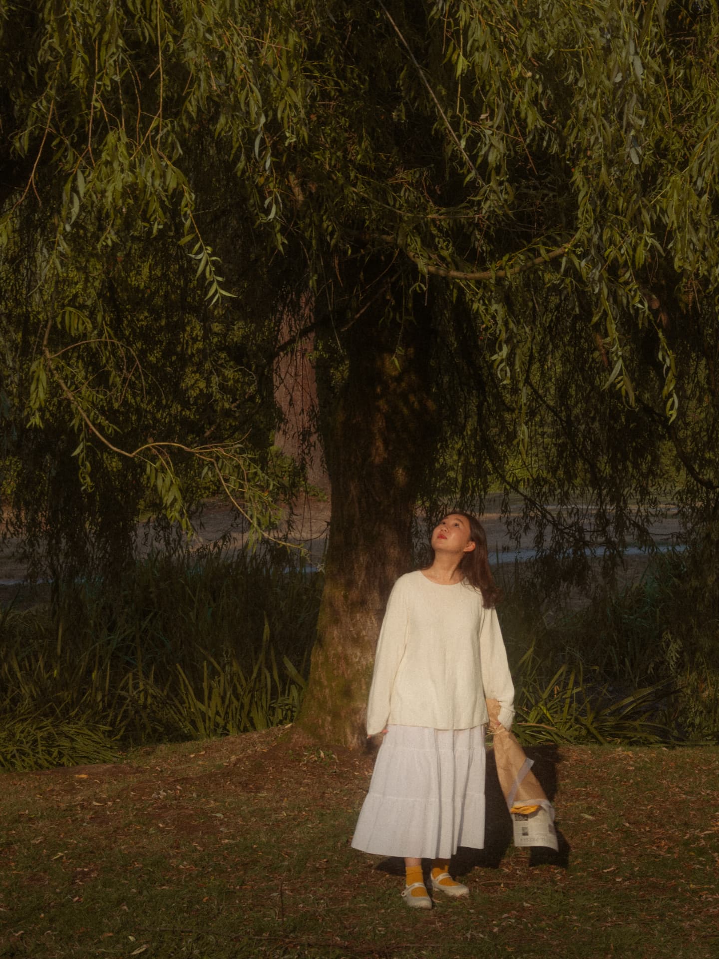 Woman looking up toward tree branches while holding flowers in an outdoor Metro Vancouver setting
