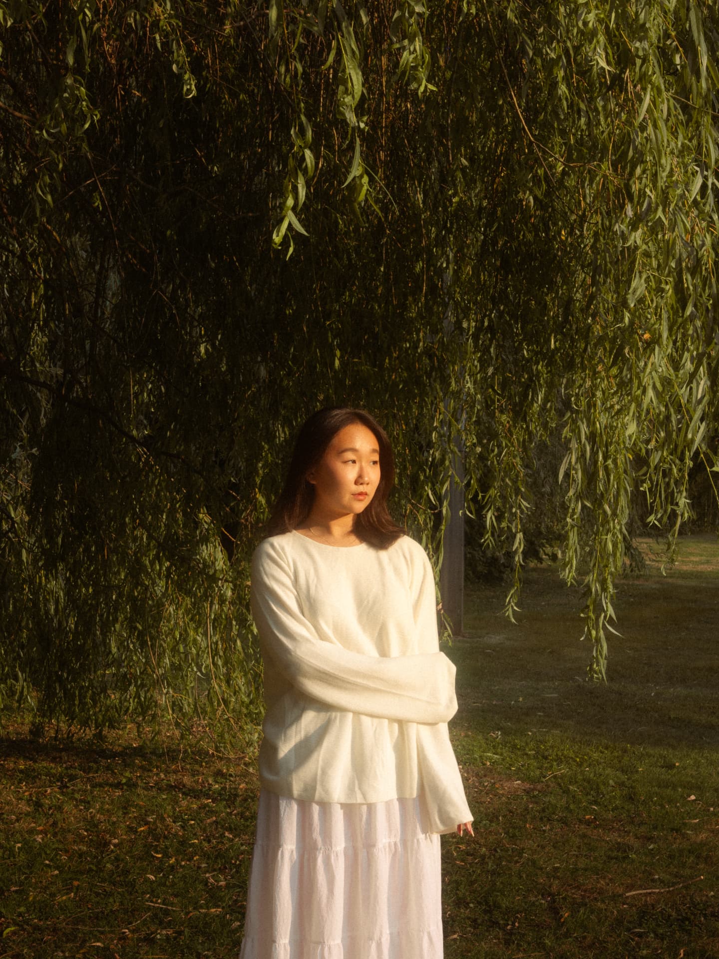Woman standing serenely beneath a weeping willow at golden hour in Metro Vancouver